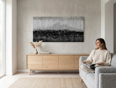 Quadro dipinto a mano con motivo a linee orizzontali astratte nei toni del bianco e nero appeso in un moderno e stiloso interno sopra una consolle in legno con vaso e candela.