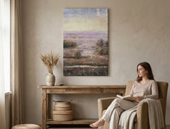 Quadro dipinto a mano con motivo paesaggio tranquillo in delicate tonalità pastello appeso in un interno moderno ed elegante sopra una consolle in legno con vaso e candela.