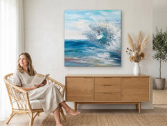 Quadro dipinto a mano con motivo mare in tempesta nei colori blu e bianco appeso in un moderno e stiloso interno sopra una consolle in legno con vaso e candela.