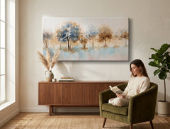 Quadro dipinto a mano con motivo paesaggio di alberi nei colori blu e marrone appeso in un interno moderno ed elegante sopra una consolle in legno con un vaso e una candela.