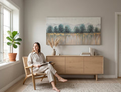 Quadro dipinto a mano su tela, motivo alberi e natura in tonalità bianco-blu, 140x70 cm, appeso in un soggiorno moderno, crea un'atmosfera rilassante.