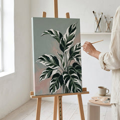 Artista nel laboratorio Papilora al lavoro su un quadro botanico con foglie tropicali, illuminato da luce naturale, qualità artigianale.
